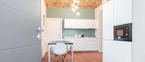 A modern kitchen with white cabinets, a wooden dining table, and a hanging light fixture.