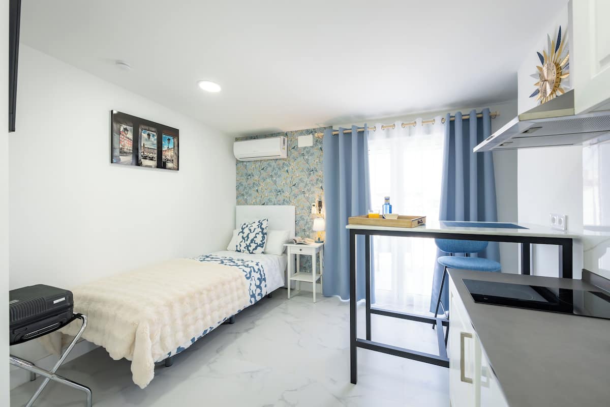 Een compacte hotelkamer met een bed, een bureau met stoel, een kleine tafel en een kitchenette.
