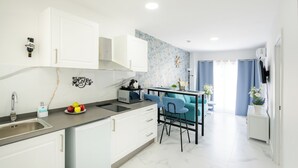 Una cocina moderna con armarios blancos, encimera de mármol y una pared de acento azul. Hay una pequeña zona de bar con dos sillas azules y una máquina de café.
