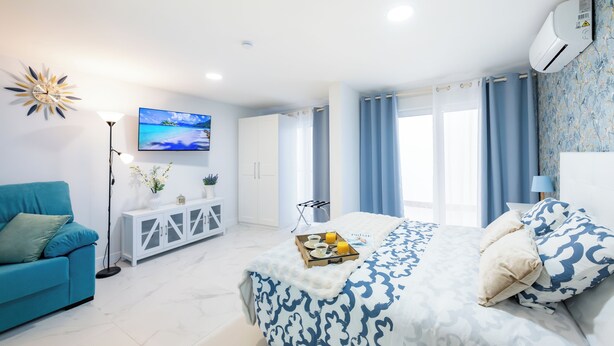 Un dormitorio moderno con una cama grande, un sofá azul, un televisor y un armario blanco.