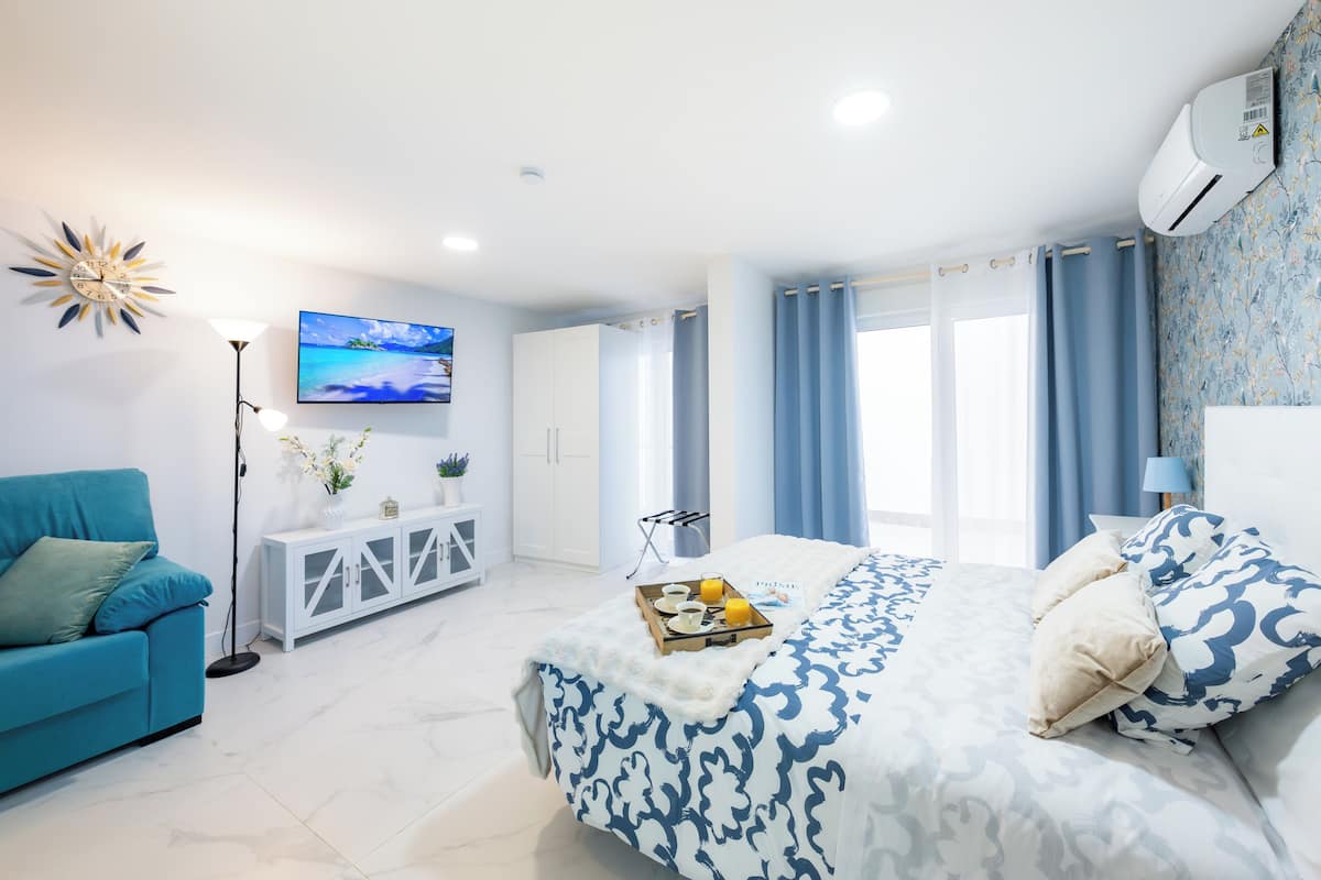 Een moderne slaapkamer met een groot bed, een blauwe bank, een televisie en een witte kast.