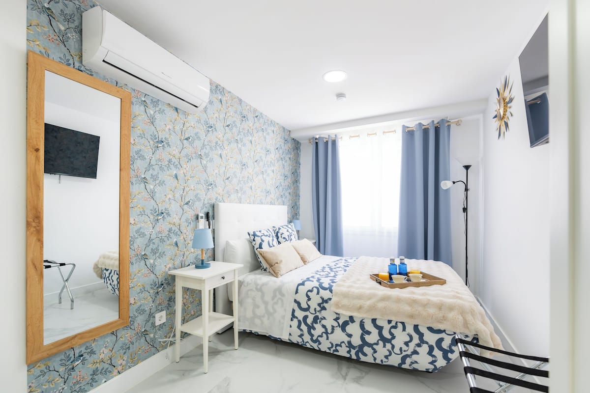 Een slaapkamer met een bed, nachtkastje, spiegel en een raam met gordijnen.