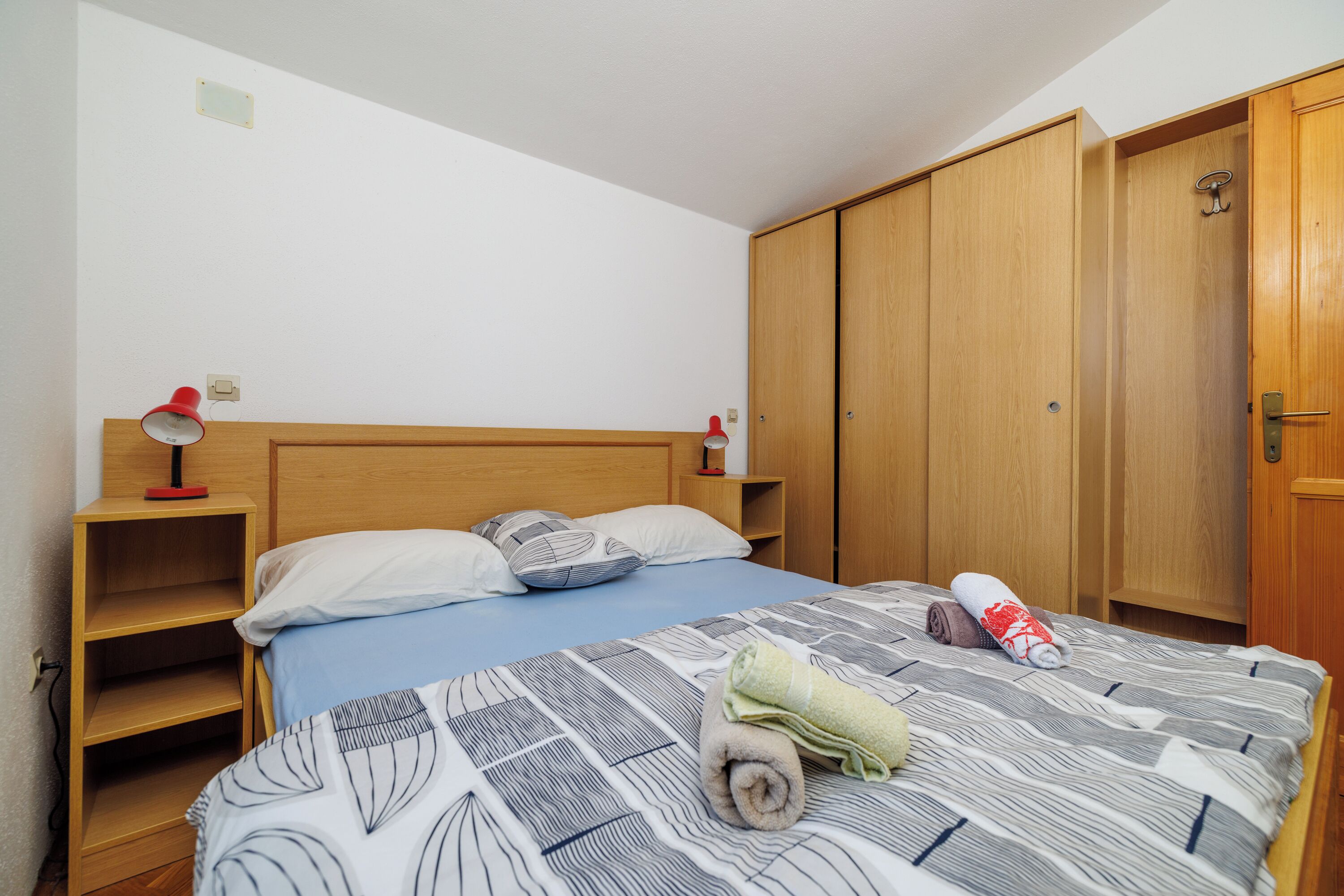 Un dormitorio con cama, armario de madera y mesita de noche con lámpara.