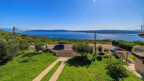 A residential area with a paved driveway leading to a house, a parked car, and a view of the sea and mountains in the background. - Apartman Mistral 4 (Crikvenica)