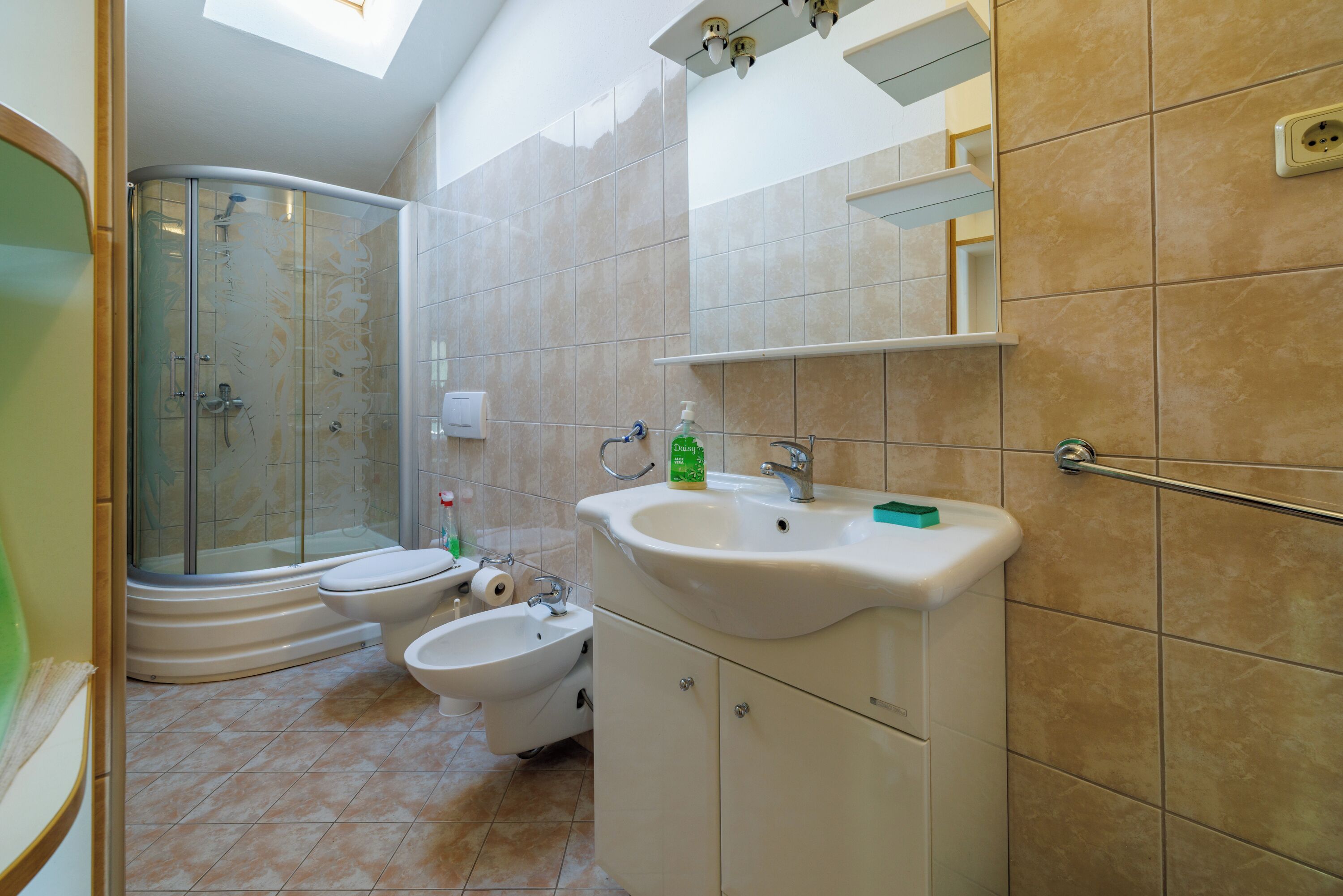 Een badkamer met douche, toilet, bidet, wastafel en een spiegel.