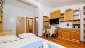 A compact room with a bed, a dining table, and wooden cabinets. - Apartman Mistral 4 (Crikvenica)