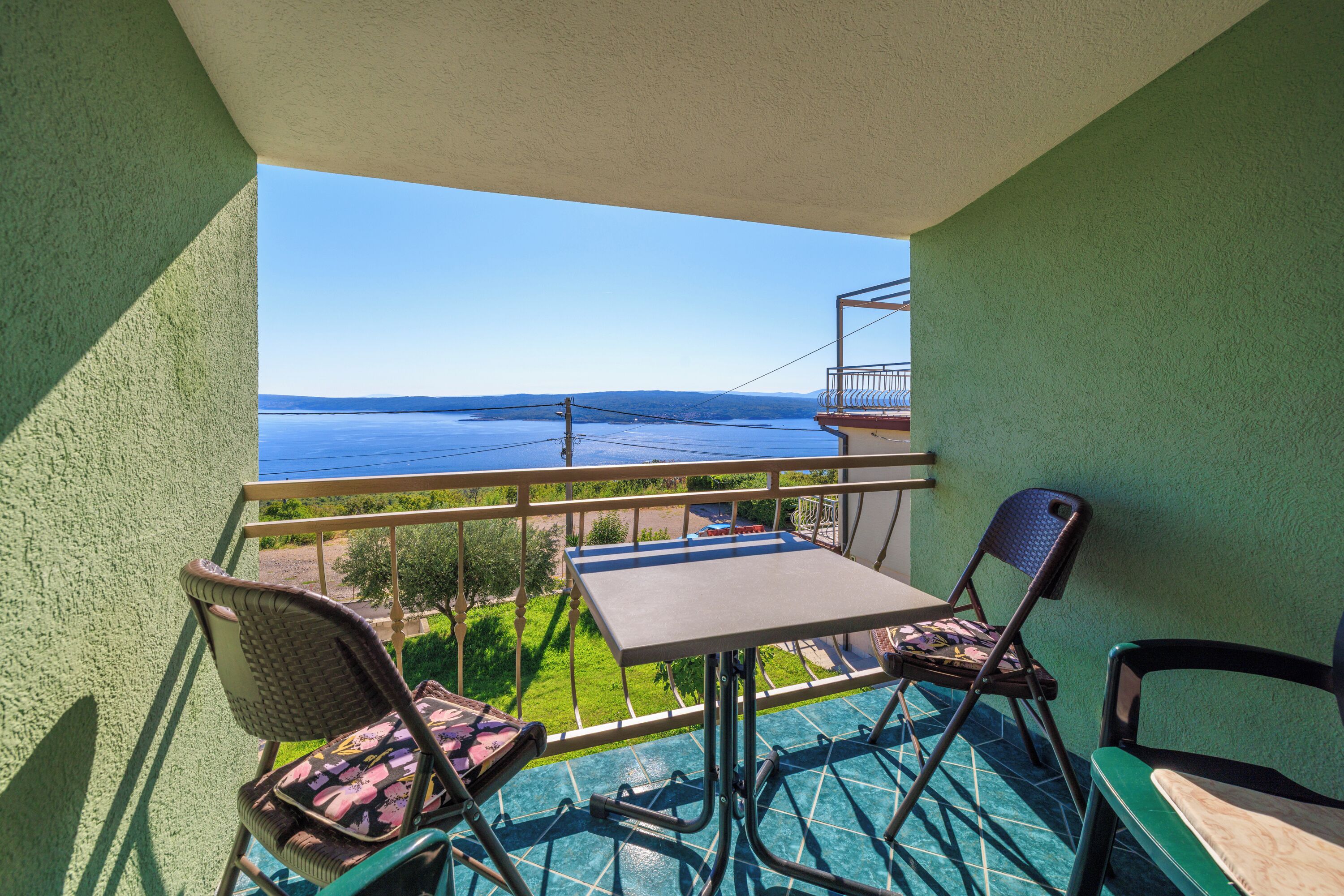 A balcony with a table and chairs, overlooking a body of water and greenery.
