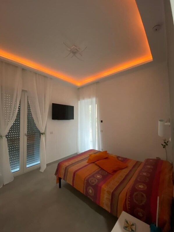 A bedroom with a bed, curtains, a TV, and a ceiling light. - Mamuccia Rooms (Naples)
