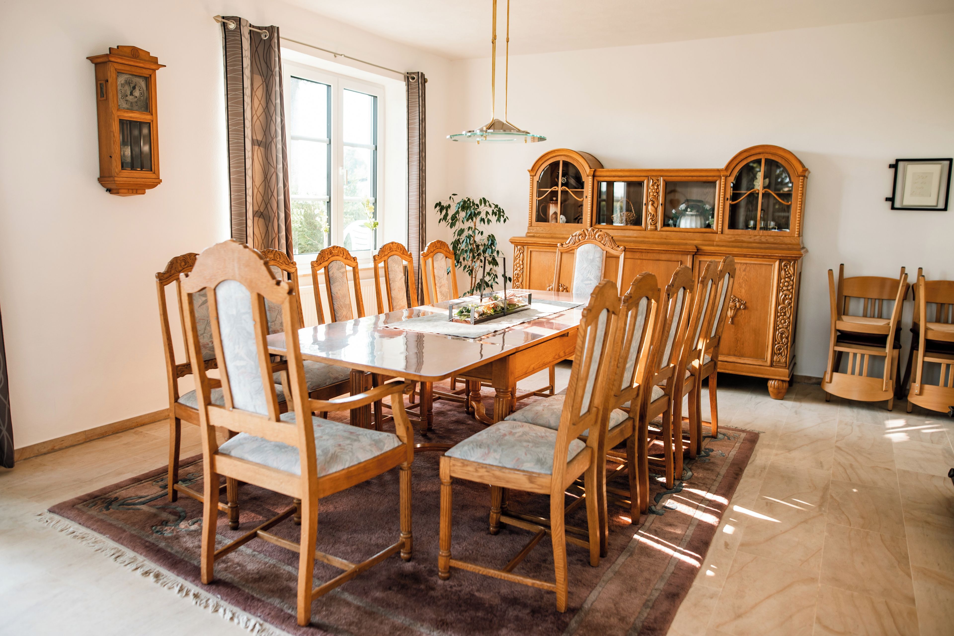 A dining room with a wooden table and chairs, a chandelier, and a wooden cabinet.