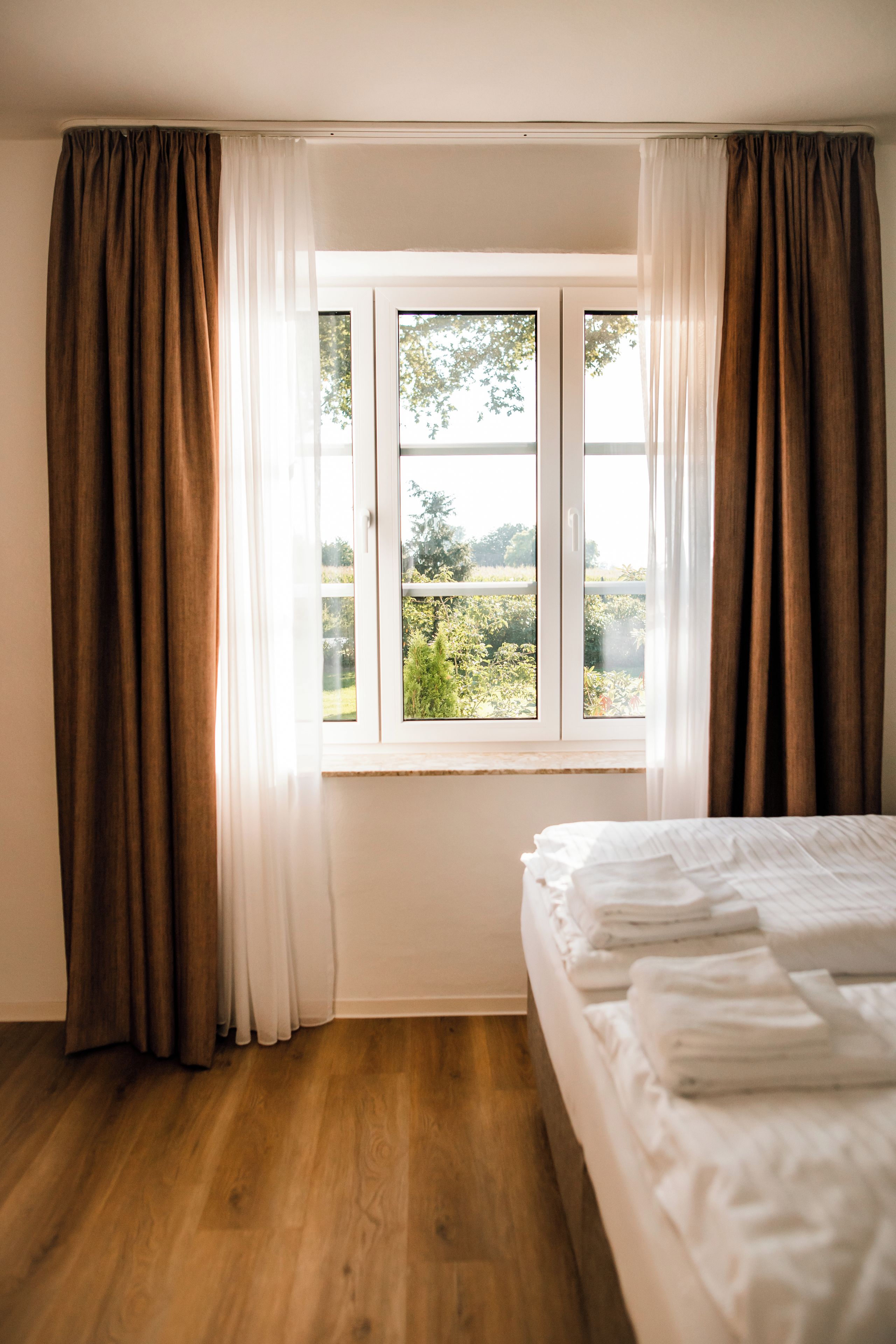A bedroom with a wooden floor, a bed with white linens, and a window with curtains.