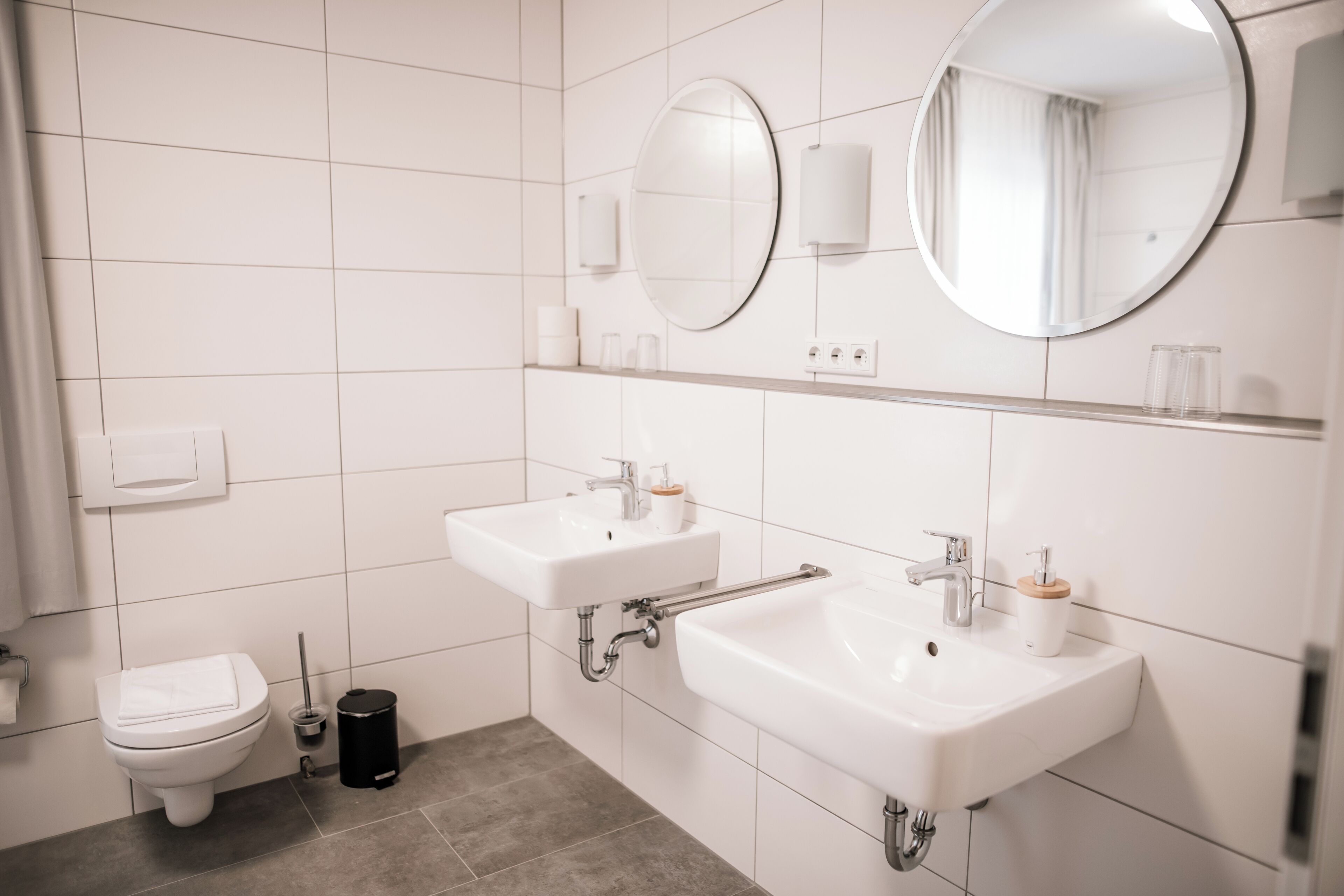A modern bathroom with two sinks, a toilet, and a mirror.