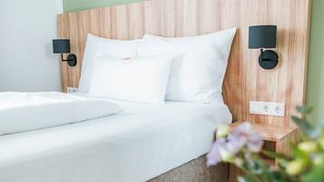 A modern hotel room with a wooden headboard, white bedding, two wall-mounted nightstands, and a potted plant.