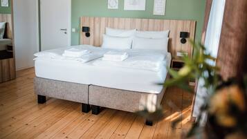 Una cama bien tendida con sábanas blancas, cabecera de madera y pared verde decorada con obras de arte.