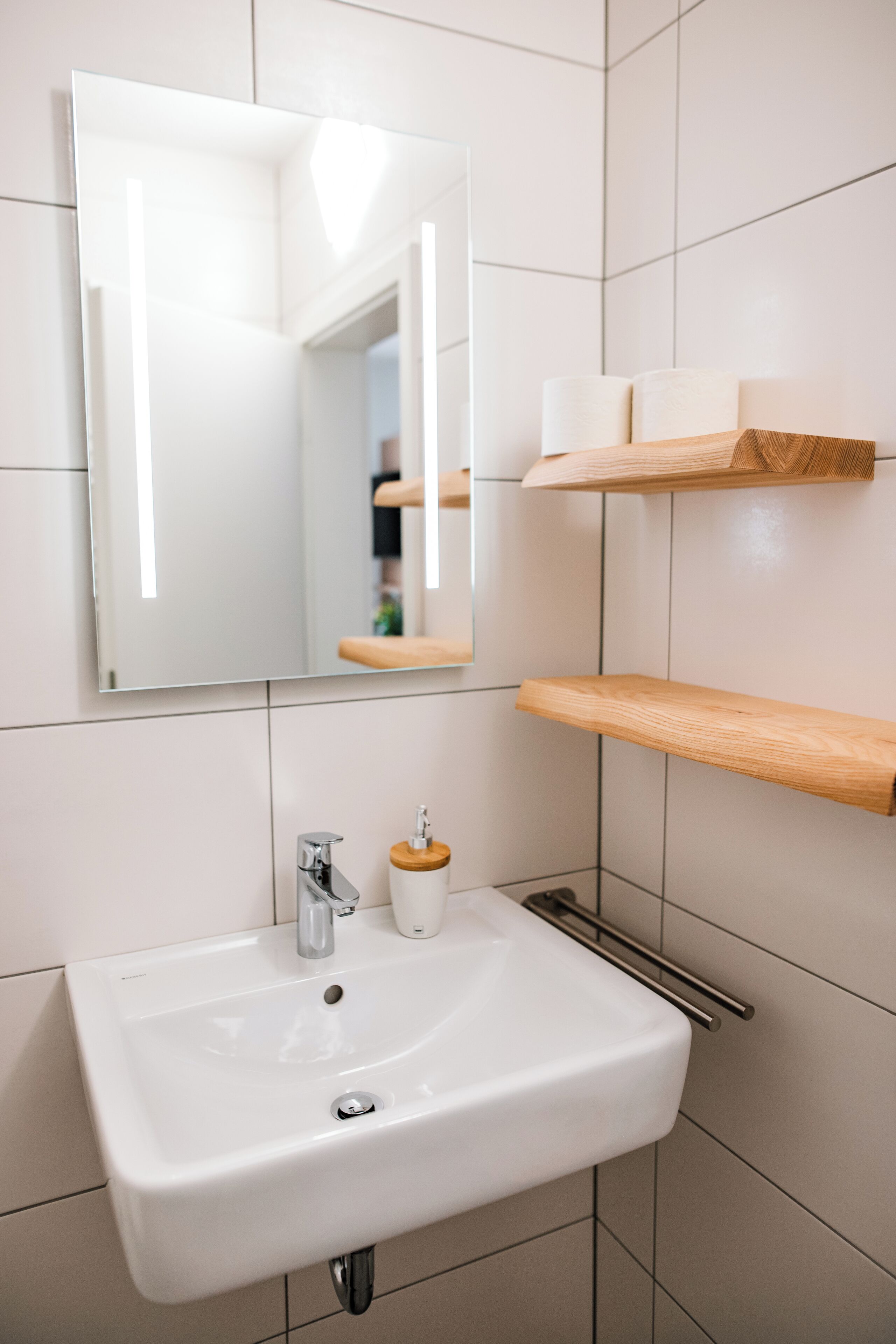 Une salle de bain avec un lavabo blanc, un miroir et des étagères en bois.