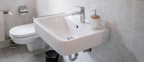 Un baño moderno con lavamanos, espejo y retrete blancos.