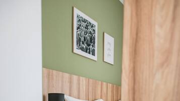 A bedroom with a wooden headboard, a white bed, a bedside table, a black lamp, and a small shelf.
