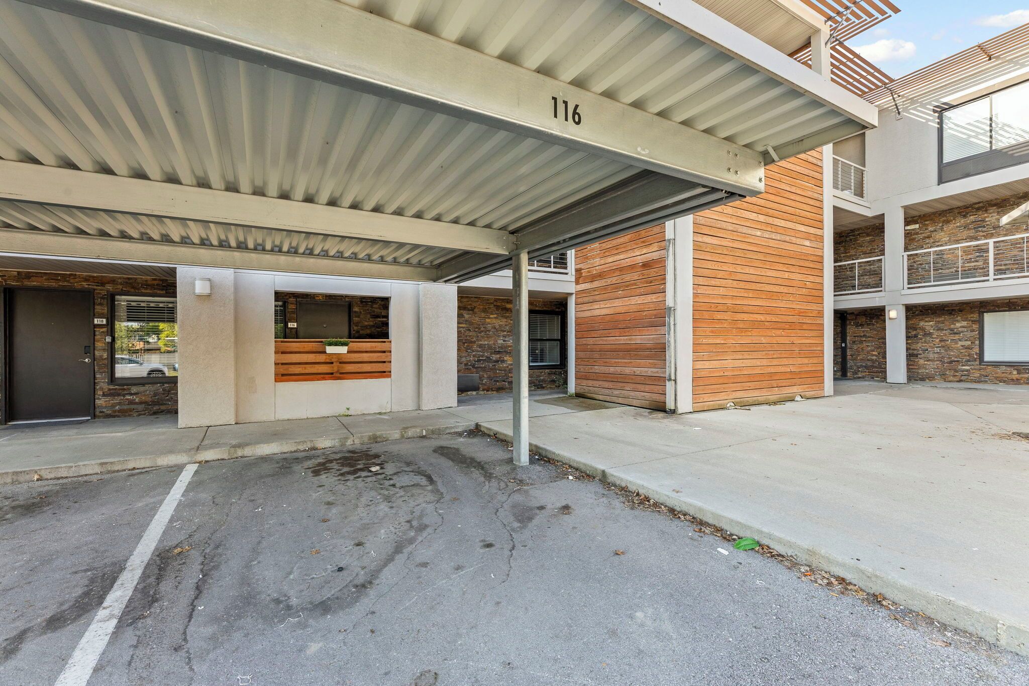 A modern building with a covered parking area, numbered 116, featuring a mix of concrete and wooden elements.