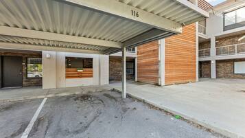 A modern building with a covered parking area, numbered 116, featuring a mix of concrete and wooden elements.