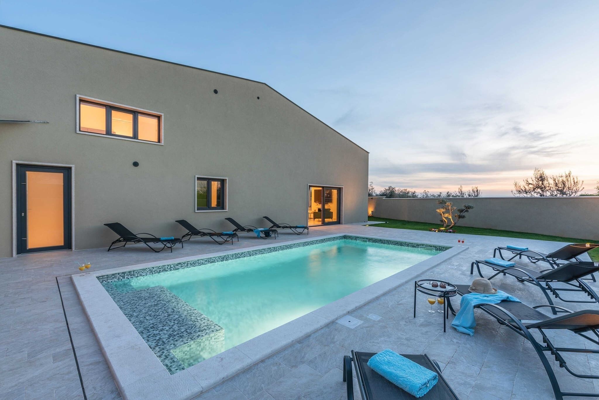 Un área de piscina moderna al aire libre con sillones de descanso y cielo despejado.