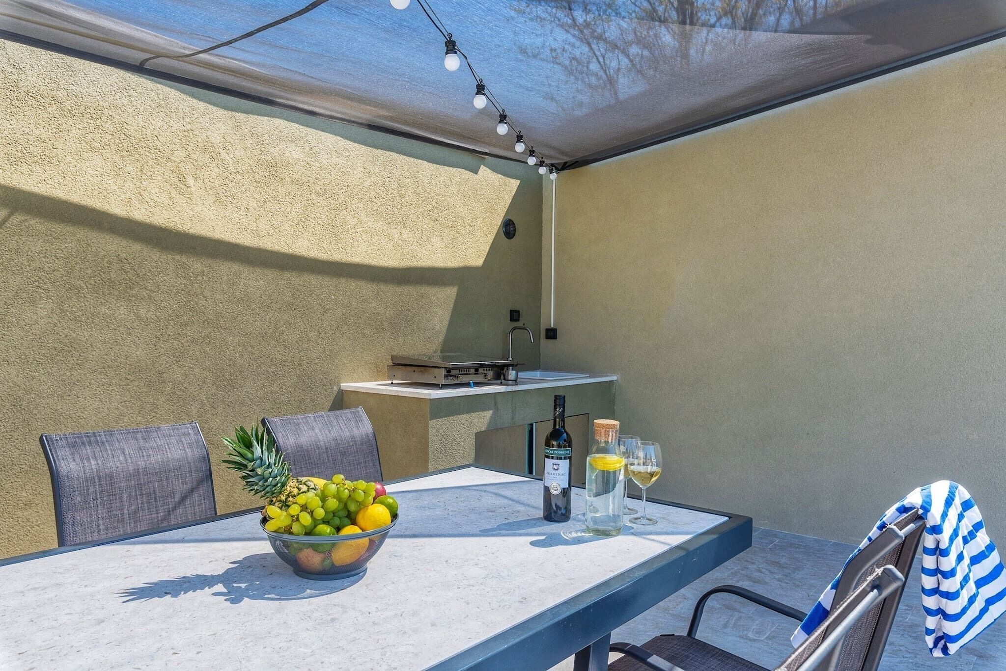 Un patio al aire libre con una mesa, sillas, un cuenco de fruta, una botella de vino y vasos.