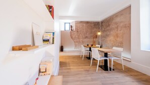 Een moderne eethoek met een houten tafel en witte stoelen, een boekenkast met boeken en een lijst, en een gestructureerde muur op de achtergrond.
