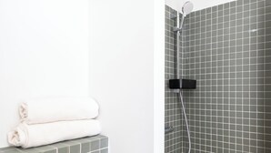Een badkamer met een betegelde douchewand, een zwarte handdoekhouder met opgevouwen handdoeken en een grijze betegelde vloer.