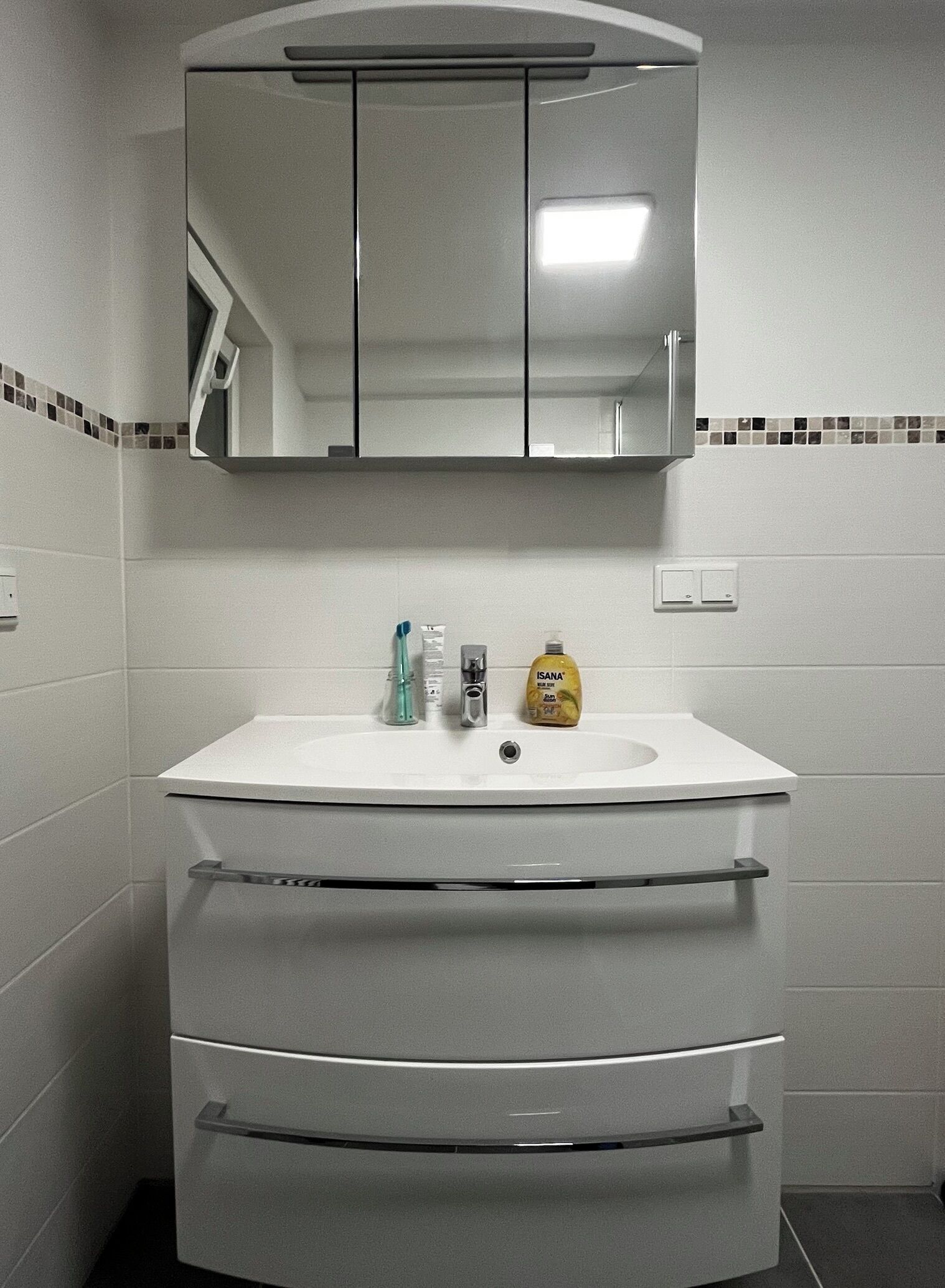 A bathroom with a white sink, a mirror above it, and a bottle of hand soap on the counter.