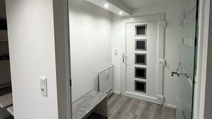 A modern, well-lit hallway with a built-in bench, a glass door, and a white door with a grid pattern. - Newly renovated basement apartment (Rodenbach)