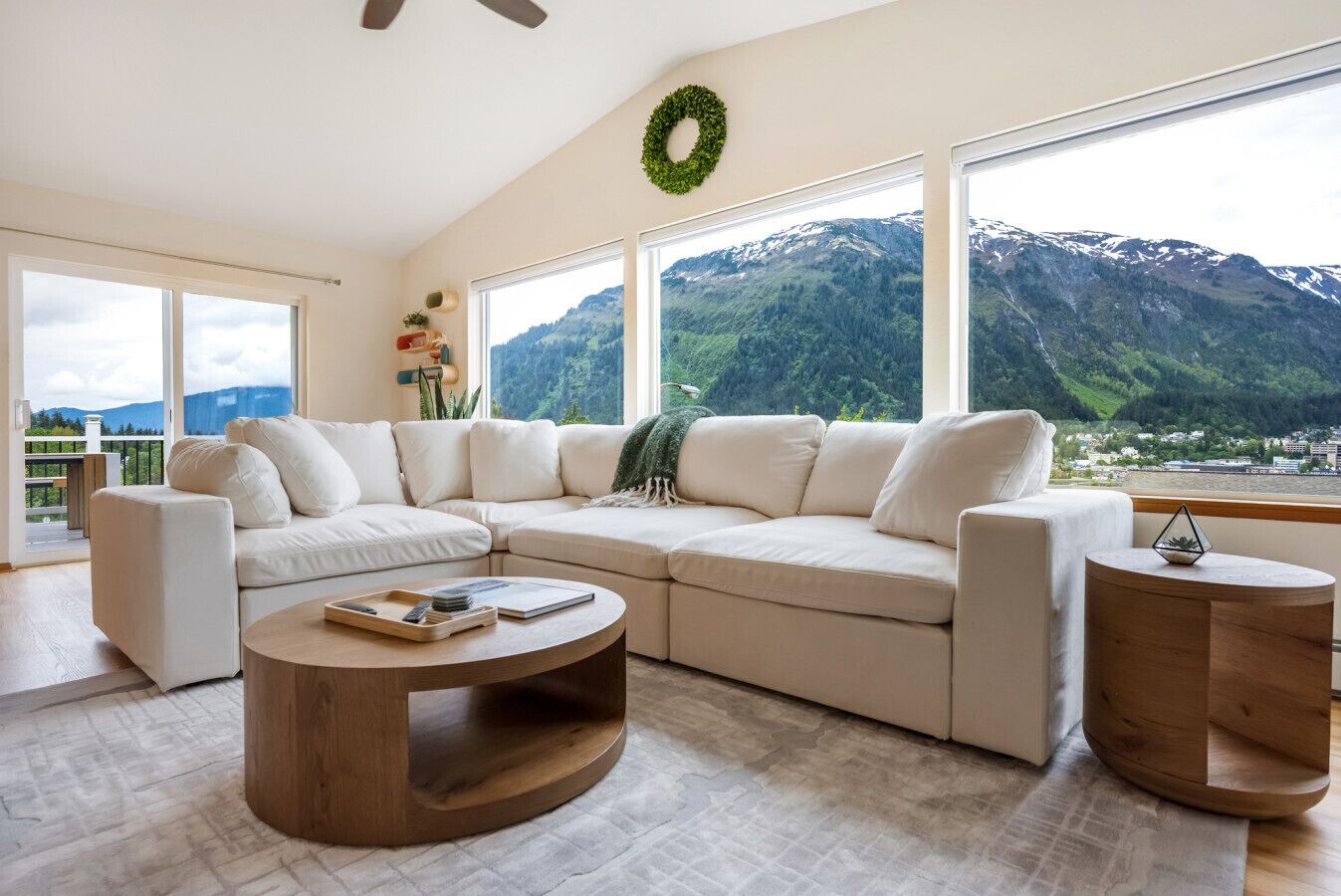 A modern living room with a sectional sofa, a round coffee table, and a view of mountains through large windows.