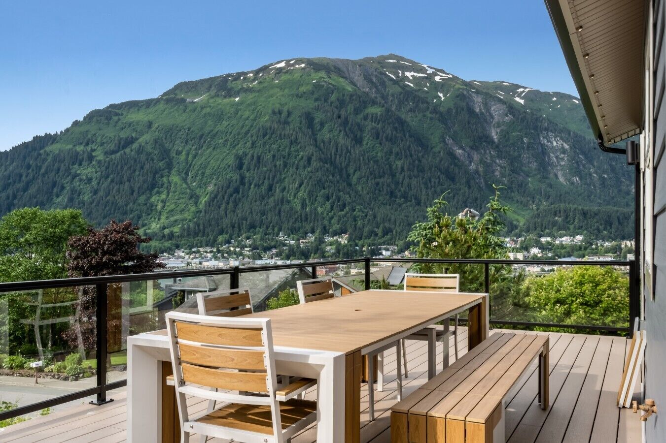 A wooden deck with a table and chairs, overlooking a mountain and a town.