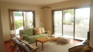 Ein großzügiges Wohnzimmer mit einem grünen Sofa, einem Holztisch und einer großen Schiebetür zu einem Innenhof mit Palmen.