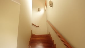Eine Holztreppe mit Handlauf, die zu einer Zwischenebene mit einer Leuchte führt.