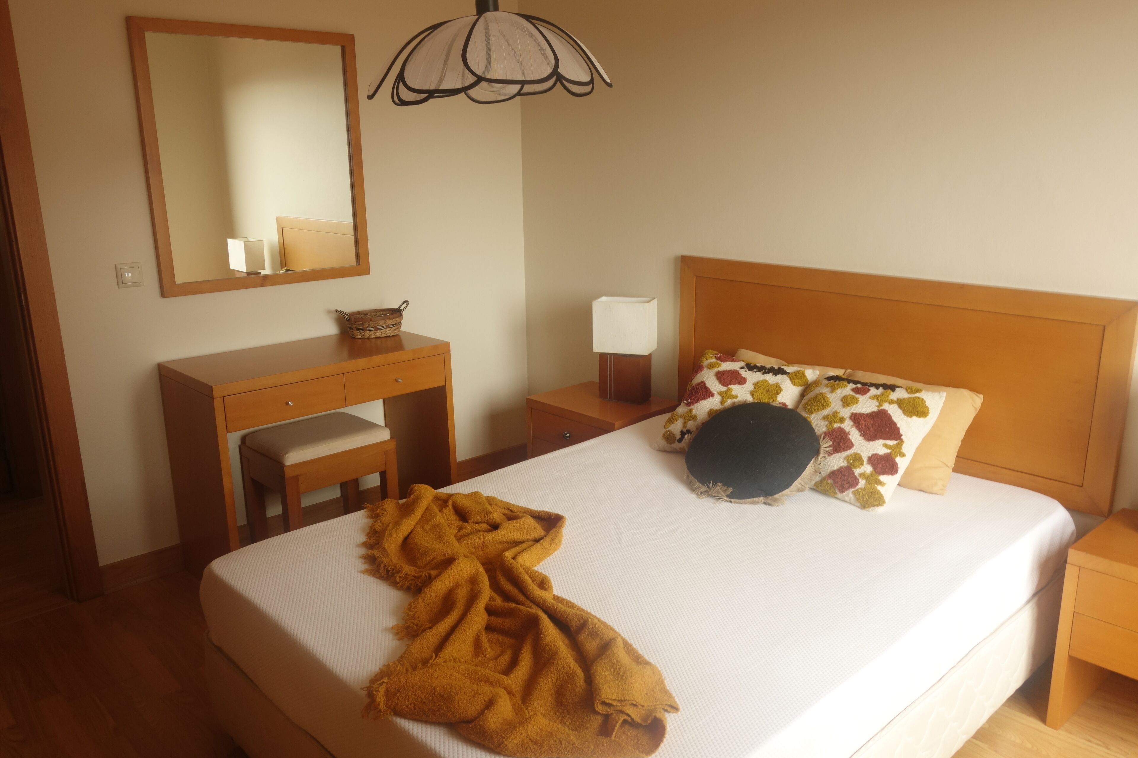 Une chambre bien rangée, avec un lit, une table de chevet, une lampe et un miroir au mur.
