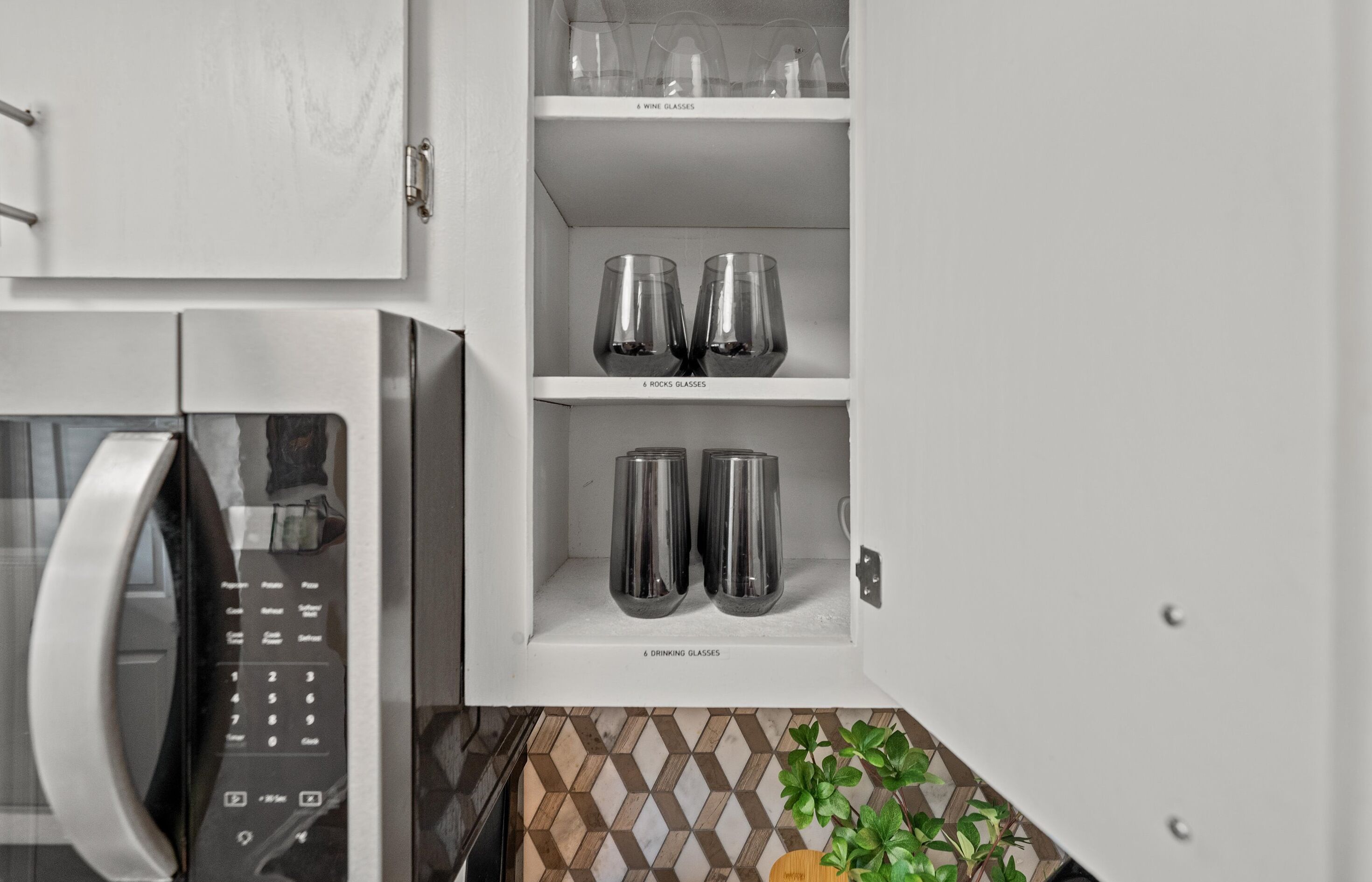 A kitchen with a microwave, wine glasses, and drinking glasses on shelves.
