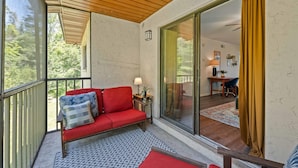 A balcony with a red sofa, a patterned rug, and a wooden ceiling.
