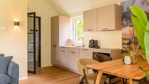 A compact kitchen with wooden cabinets, a window, and a dining area with a table and chairs. - Detached wellness accommodation for 4 people (Gasselte)
