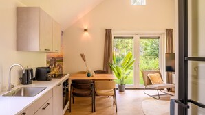 A modern kitchen with a dining area, a large window with curtains, and a view of greenery outside. - Detached wellness accommodation for 4 people (Gasselte)