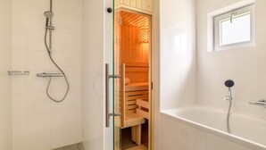 A modern bathroom with a glass-enclosed sauna, a separate shower area, and a bathtub. - Detached wellness accommodation for 4 people (Gasselte)