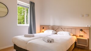 A double bed with white linens and two rolled towels, a wooden headboard, bedside lamps, and a window with curtains. - Detached wellness accommodation for 4 people (Gasselte)