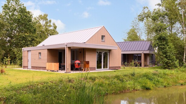 Een modern huis met twee verdiepingen, een overdekte patio en een vijver op de voorgrond.
