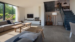 A modern living room with a sofa, coffee table, and a fireplace. There is a staircase leading to an upper level. - Watervilla Meerzicht 8 (Arnemuiden)