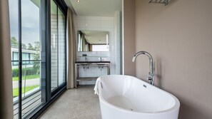 Un baño moderno con una bañera independiente, un tocador con cristal y un amplio ventanal con vistas al exterior.