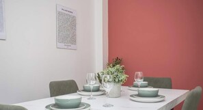 A dining table with green plates and glasses, a white vase with flowers, and a framed picture on the wall.