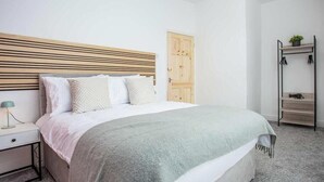 A bedroom with a bed, bedside table, lamp, wardrobe, and a small shelf with a plant.