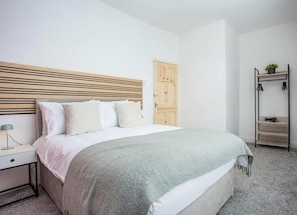 A bedroom with a bed, bedside table, lamp, wardrobe, and a small shelf with a plant. - Meldon Terrace | Parking | Wi-Fi (Northumberland)