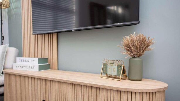 A reception desk with a mounted TV, a vase with dried plants, and a calendar.