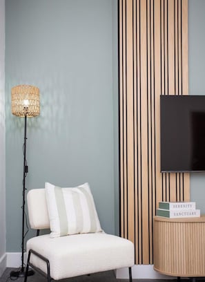 A room with a white chair, a floor lamp, a TV on the wall, and a vertical wooden panel.