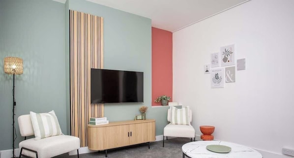 A modern living room with a flat-screen TV, a wooden cabinet, two white armchairs, a small table, and a floor lamp. - Meldon Terrace | Parking | Wi-Fi (Northumberland)