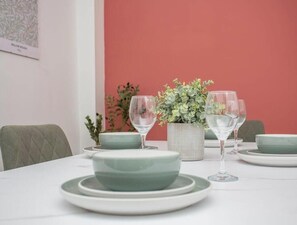 A dining table set with green plates, clear wine glasses, and a potted plant.