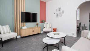 A modern living room with a flat-screen TV, a wooden cabinet, a white sofa, a round coffee table, and a small orange bowl.